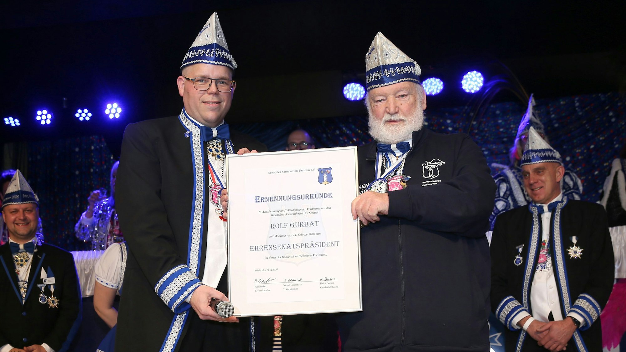 Ein Senatspräsident im Karneval verleiht einem anderen Mann eine Urkunde zum Ehren-Senatspräsidenten.