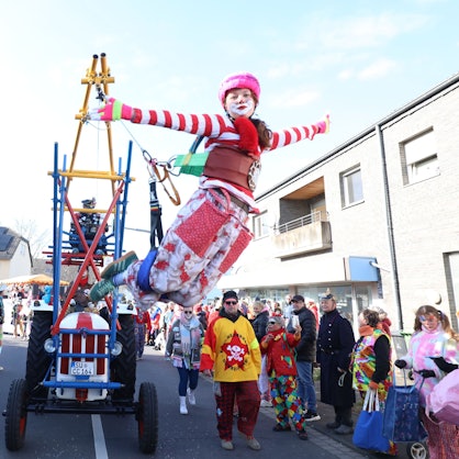 Ein bunter Clown hängt an einer Konstruktion an einem Traktor und „fliegt“ so im Karnevalszug in Bad Honnef.