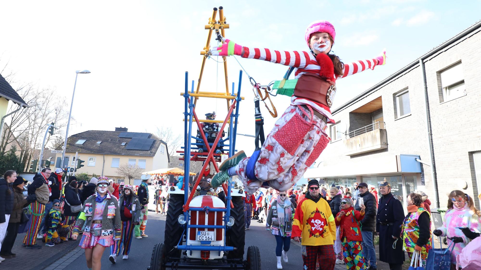 Ein bunter Clown hängt an einer Konstruktion an einem Traktor und „fliegt“ so im Karnevalszug in Bad Honnef.