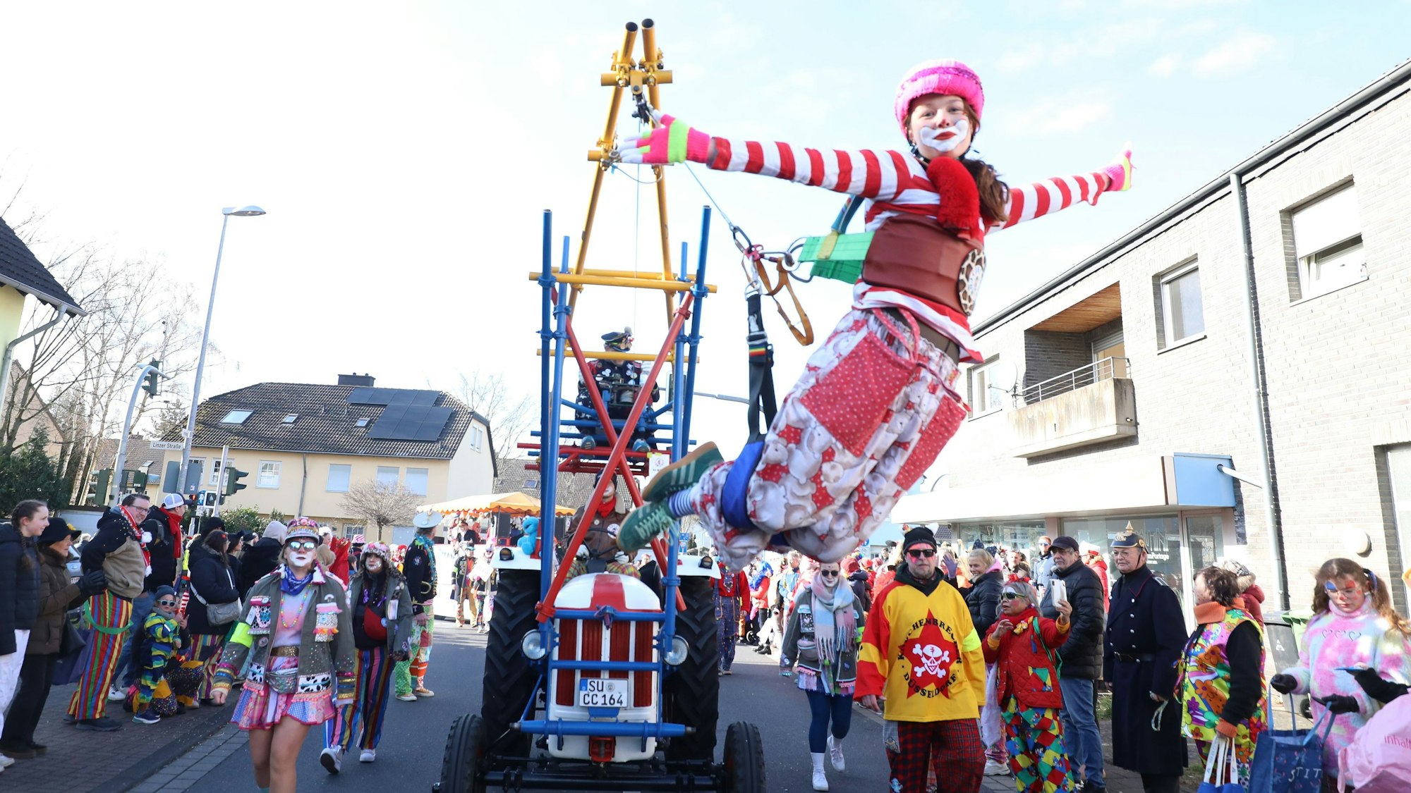Ein bunter Clown hängt an einer Konstruktion an einem Traktor und „fliegt“ so im Karnevalszug in Bad Honnef.