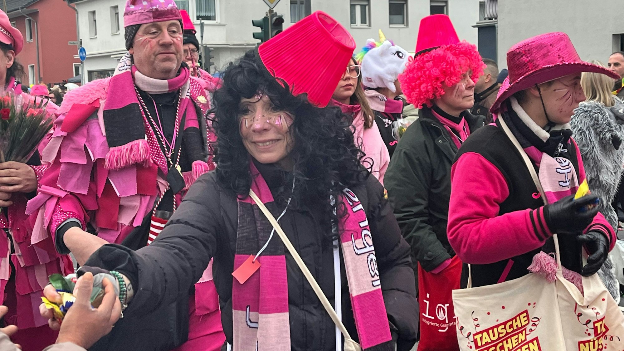 Eine Zugteilnehmerin mit pinkem Schal und schwarzer Perücke verteilt Kamelle.