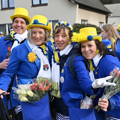Eine Gruppe Karnevalisten trägt einen blau-gelben Anzug und hat Strüssjer und eine Flasche Bier dabei.
