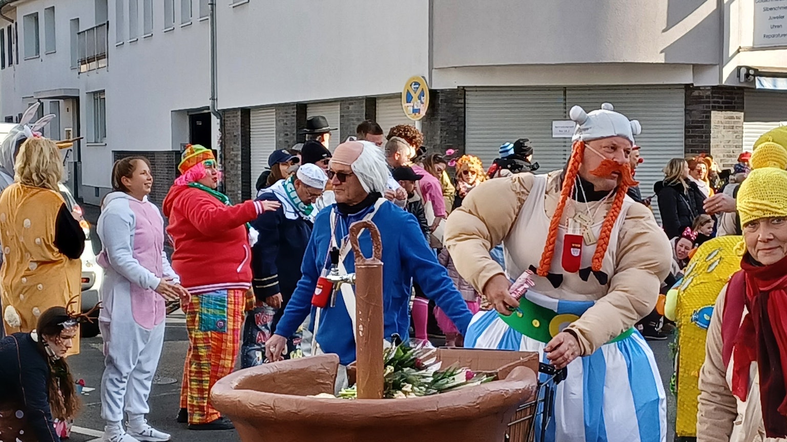 Ein als Obelix verkleideter Mann hat einen Wagen in Form eines Kessels Zaubertrank dabei. Darin sind Strüßjer.
