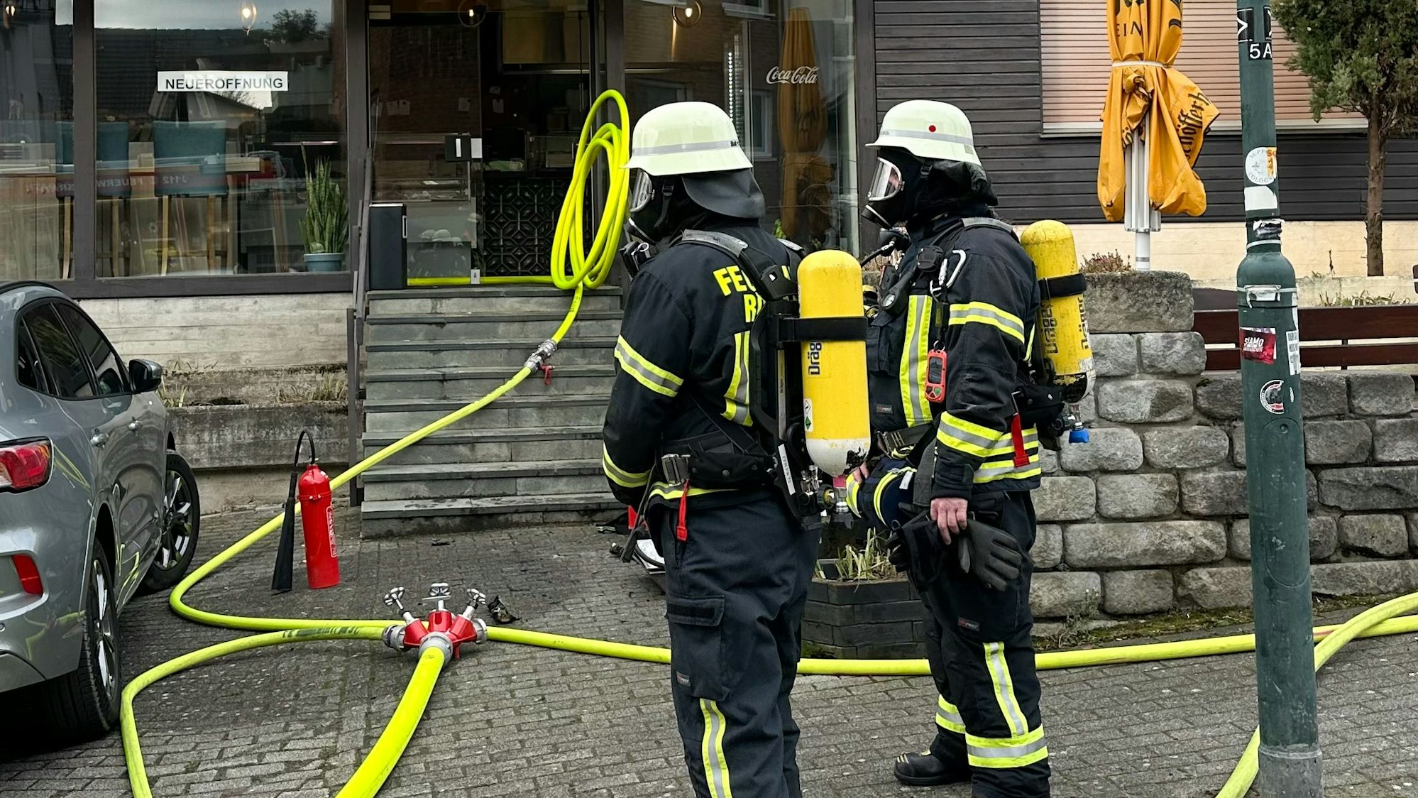 Feuerwehrleute stehen vor einem Ladenlokal, Schläuche führen hinein.