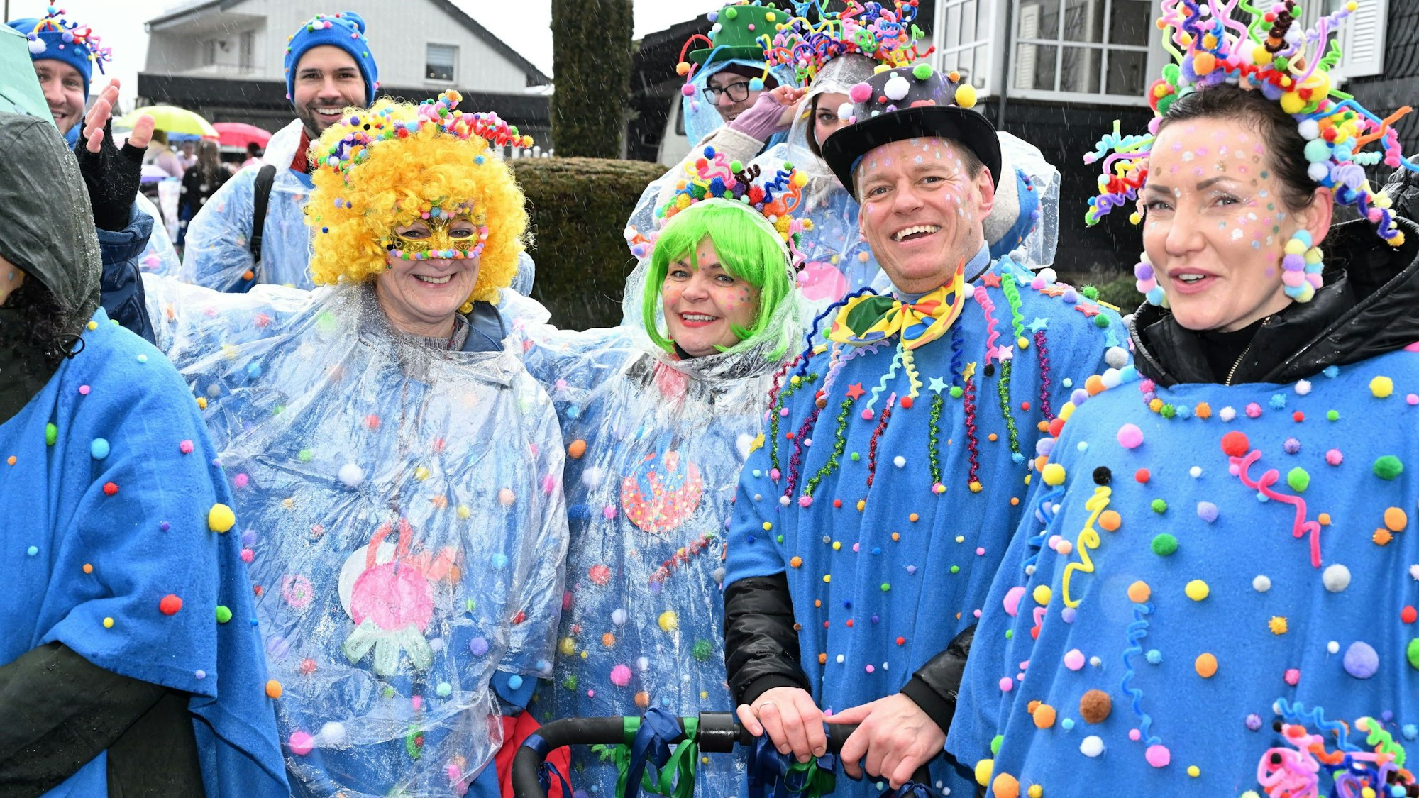 Eine Karnevalsgruppe in einem Zug. Ihre blauen Kostüme mit bunten Punkten haben sie mit Regenfolien geschützt.