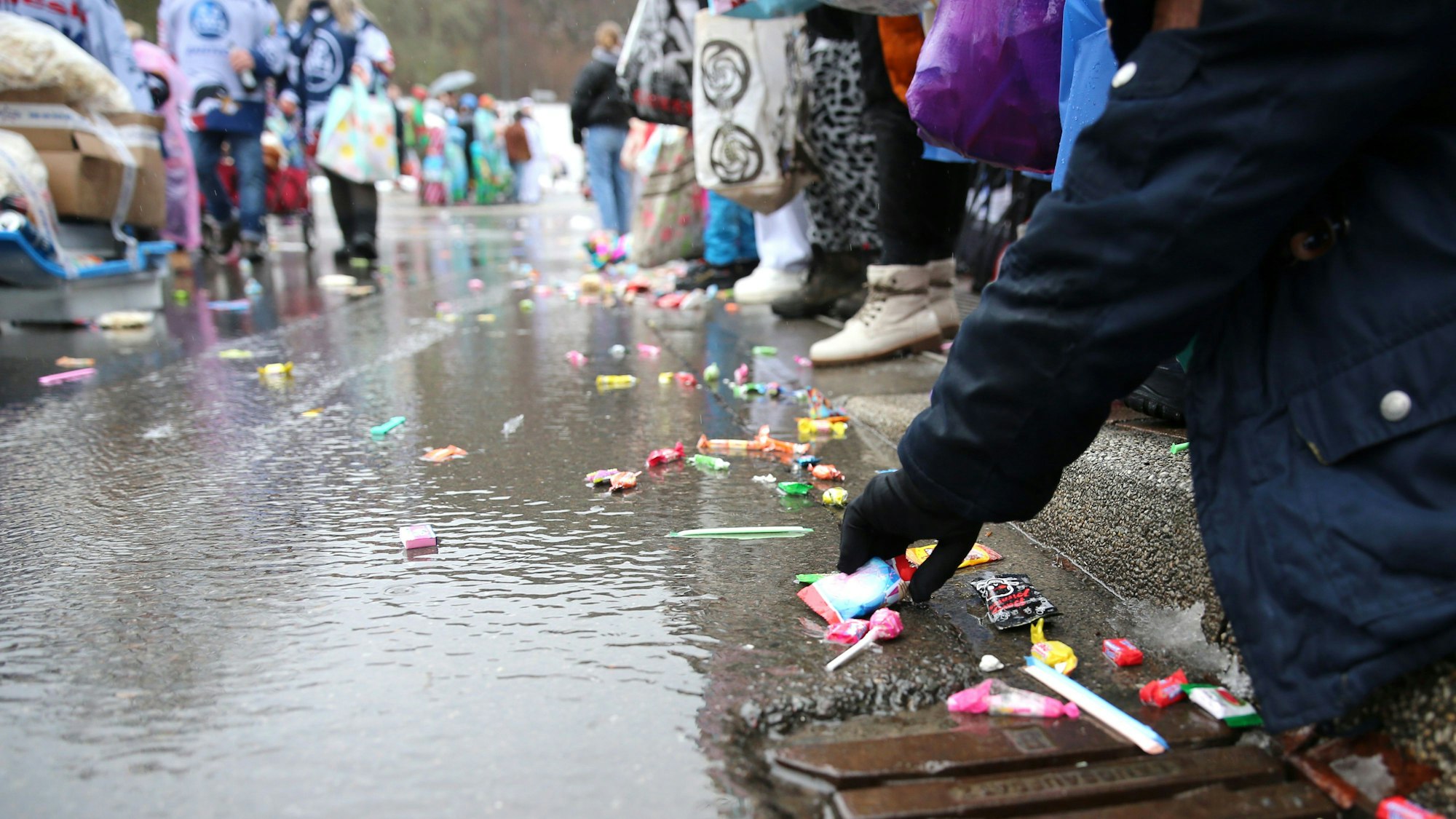 Einige Jecke fischen Kamelle aus einer Pfütze auf der Straße.