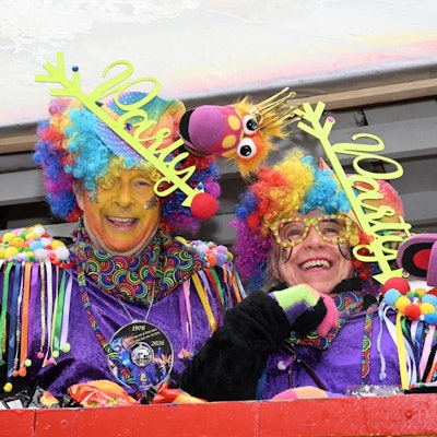 Zwei Karnevalisten in bunten Perücken und lilafarbenen Gewändern lachen in die Kamera.