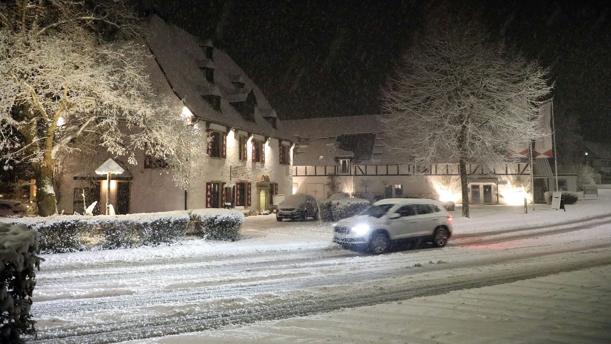 Ein Auto fährt auf einer schneebedeckten Straße an der Malteser Komturei in Bergisch Gladbach-Herrenstrunden vorbei.