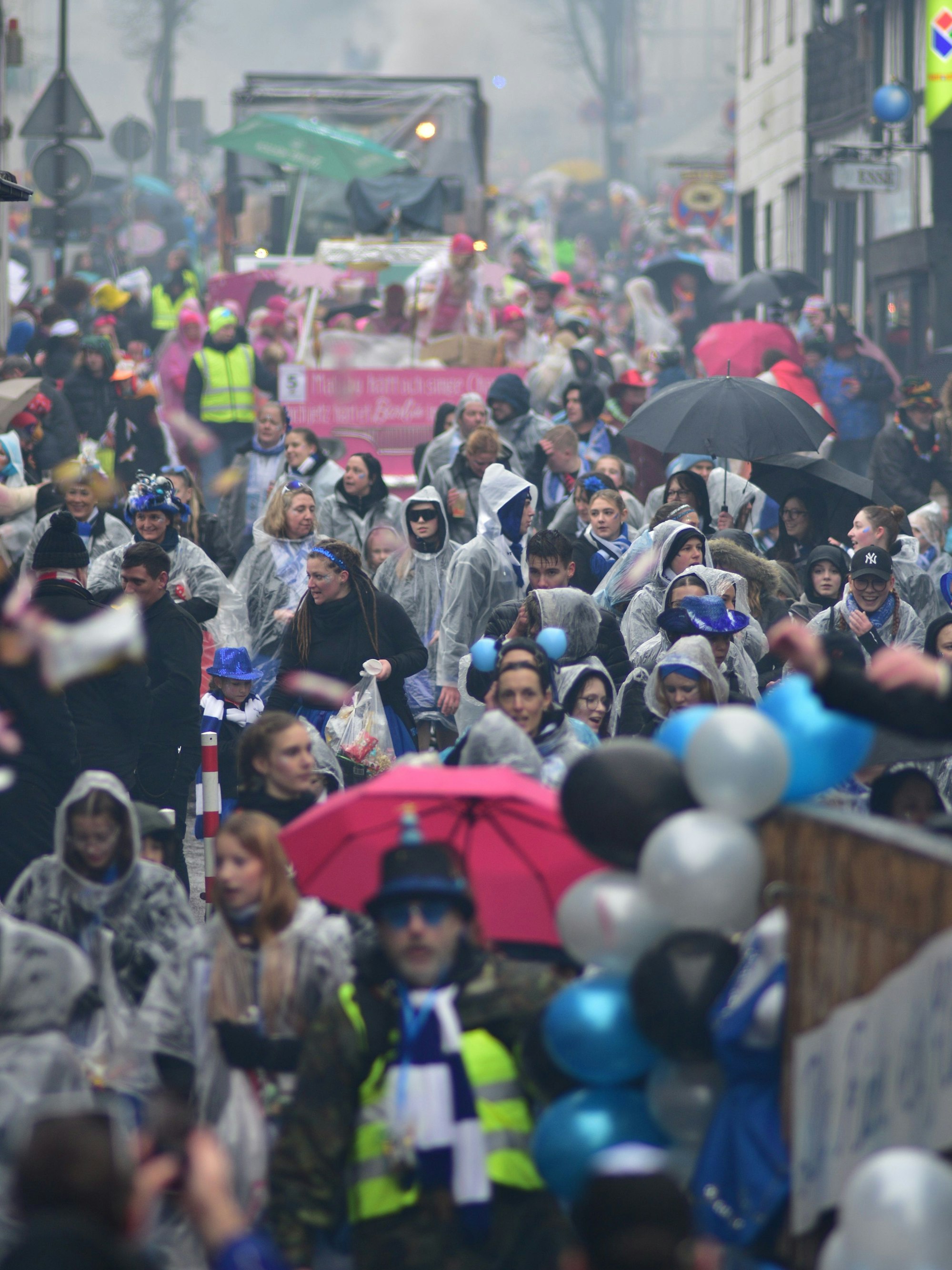 Verregneter Rosenmontagszug in Much: Die Mucher Hauptstraße ist mit Jecken unter Regenponchos und Schirmen gesäumt.