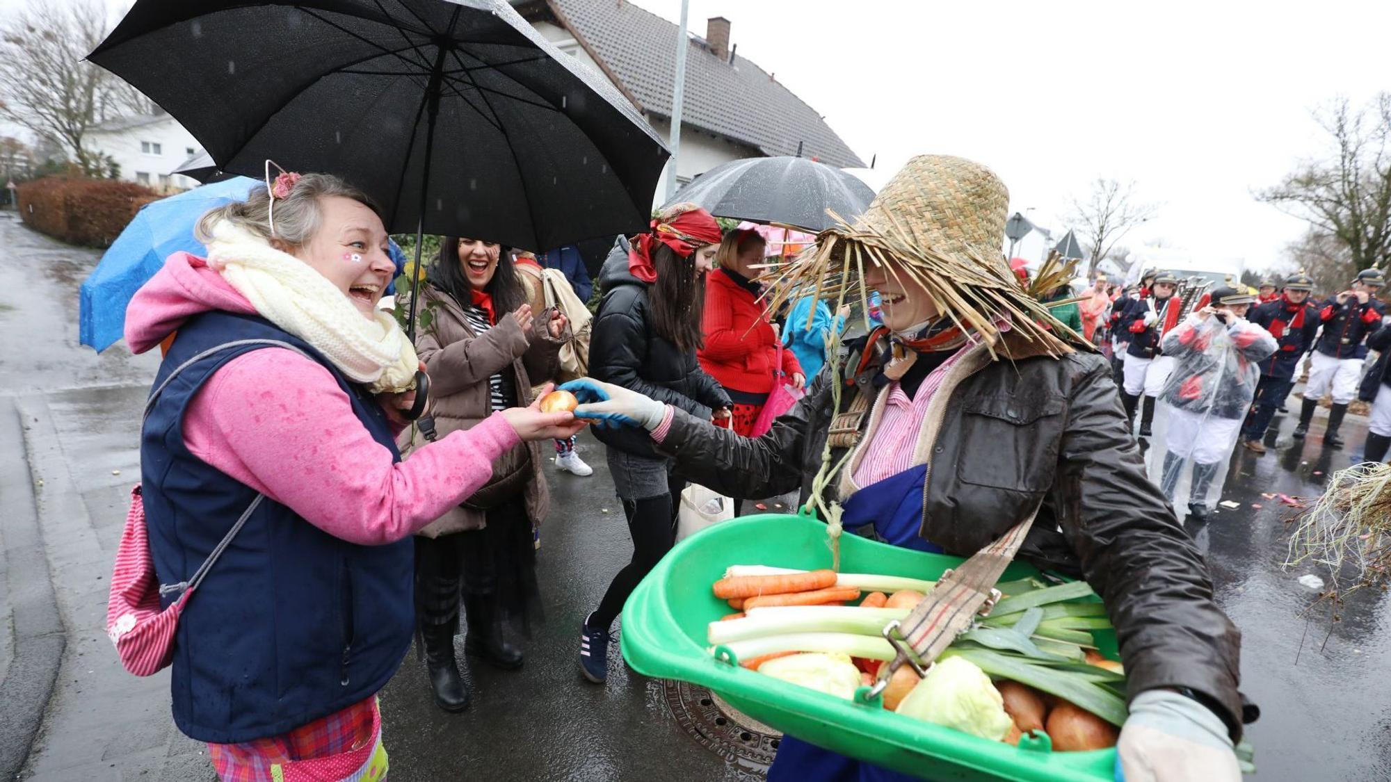 Eine Karnevalistin verteilt Obst und Gemüse an die Menschen am Straßenrand.