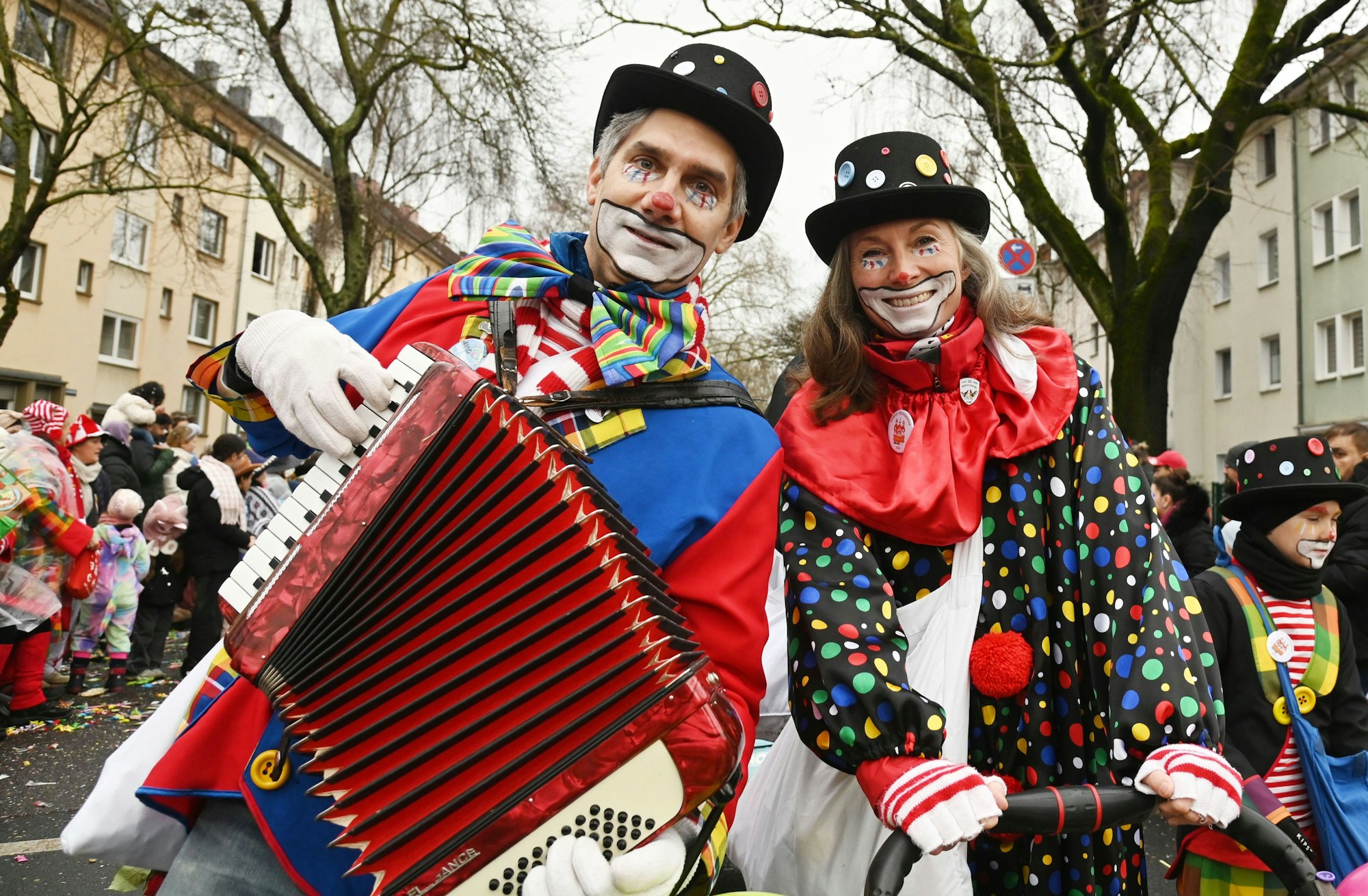Ein Paar ist als bunte Clowns verkleidet. Der Mann hat eine Quetsch dabei.