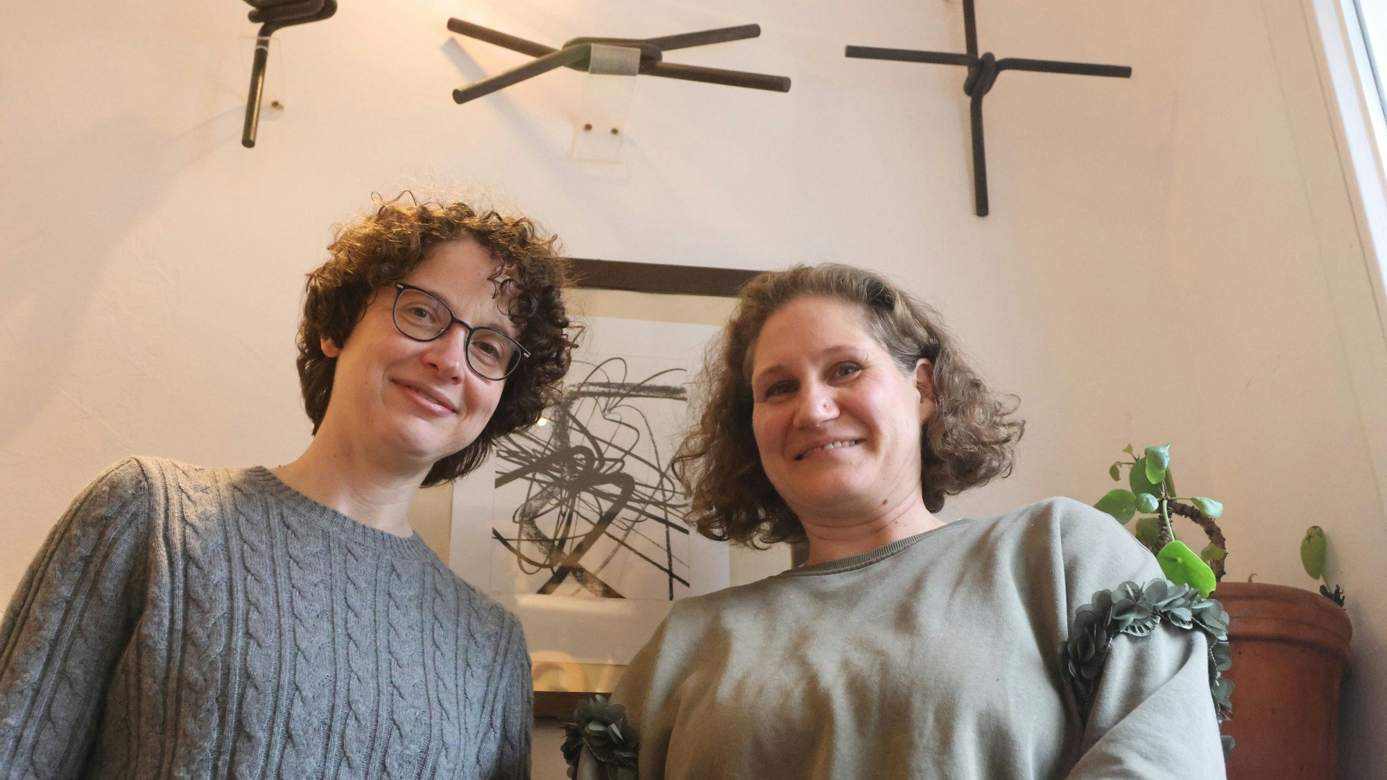 Zwei Frauen vor einer Wand mit kleinen Kunstwerken.