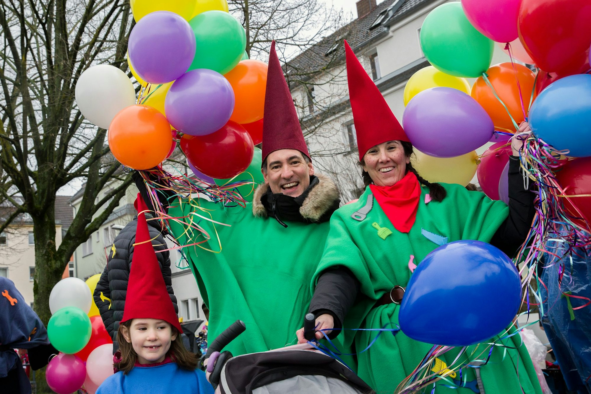 Eine Zwergenfamilie mit bunten Luftballons schauen in die Kamera.