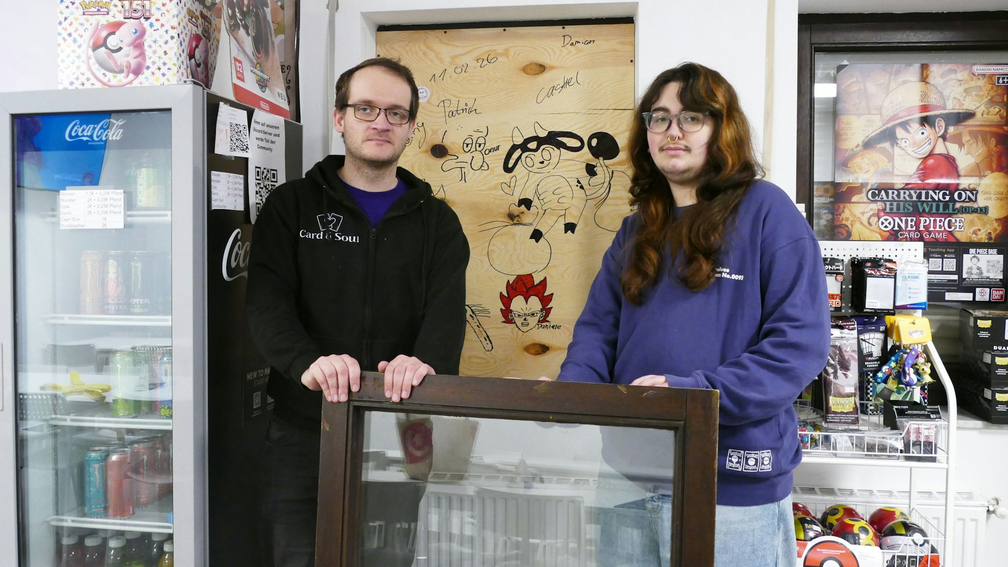 Patrick Overkamp und Castiel Heidenreich, die beiden Inhaber des Card & Soul, stehen vor dem Fenster, das der oder die Einbrecher herausgebrochen hatten.