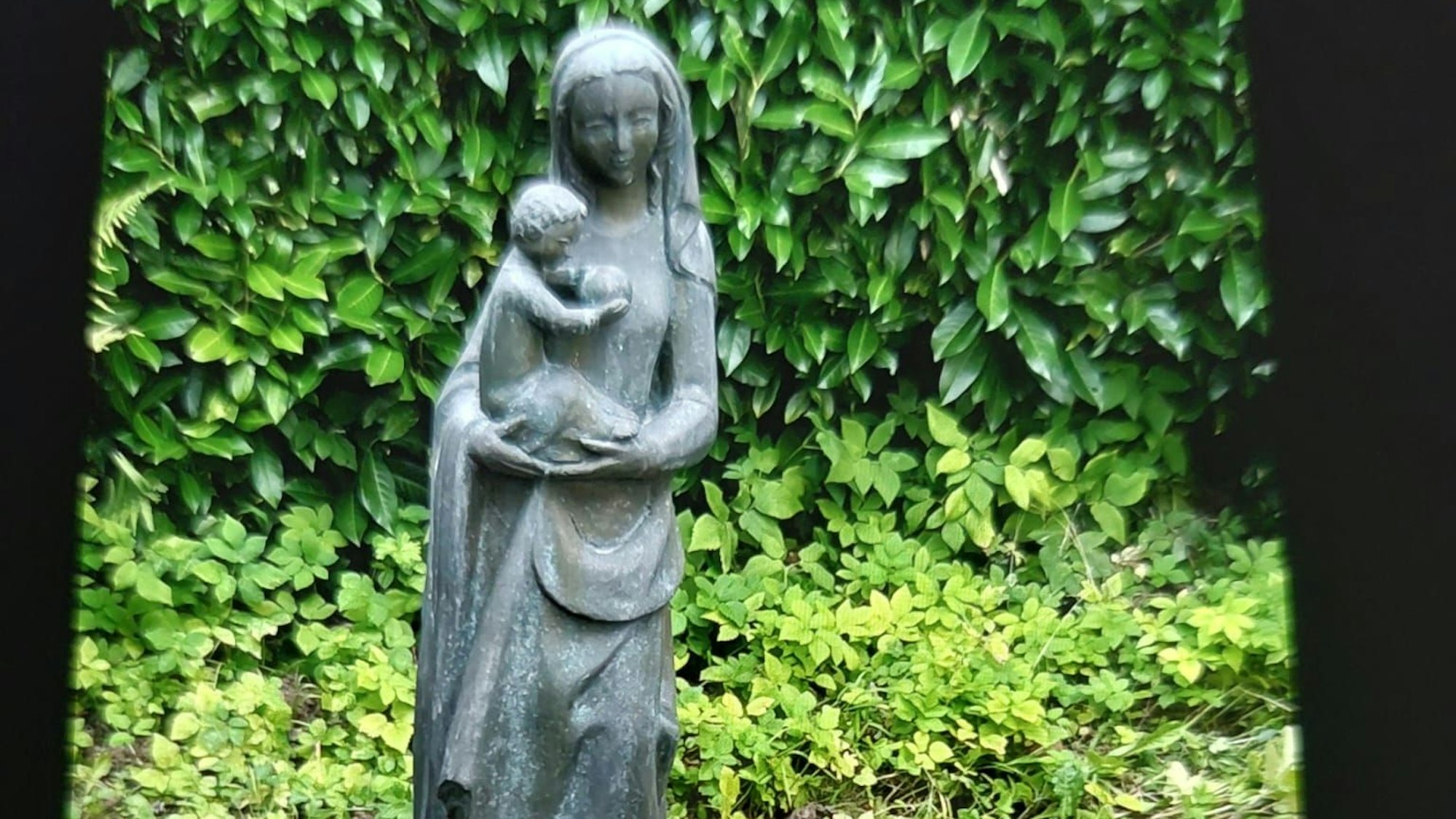 Eine Madonnenfigur aus Bronze mit Kind auf einem Friedhof.