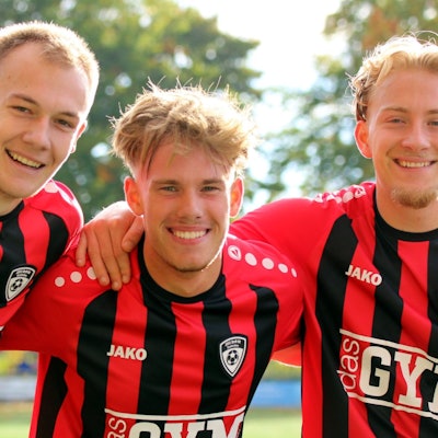 Drei Fußballer der JSG Erft 01 posieren Arm in Arm für die Kamera.