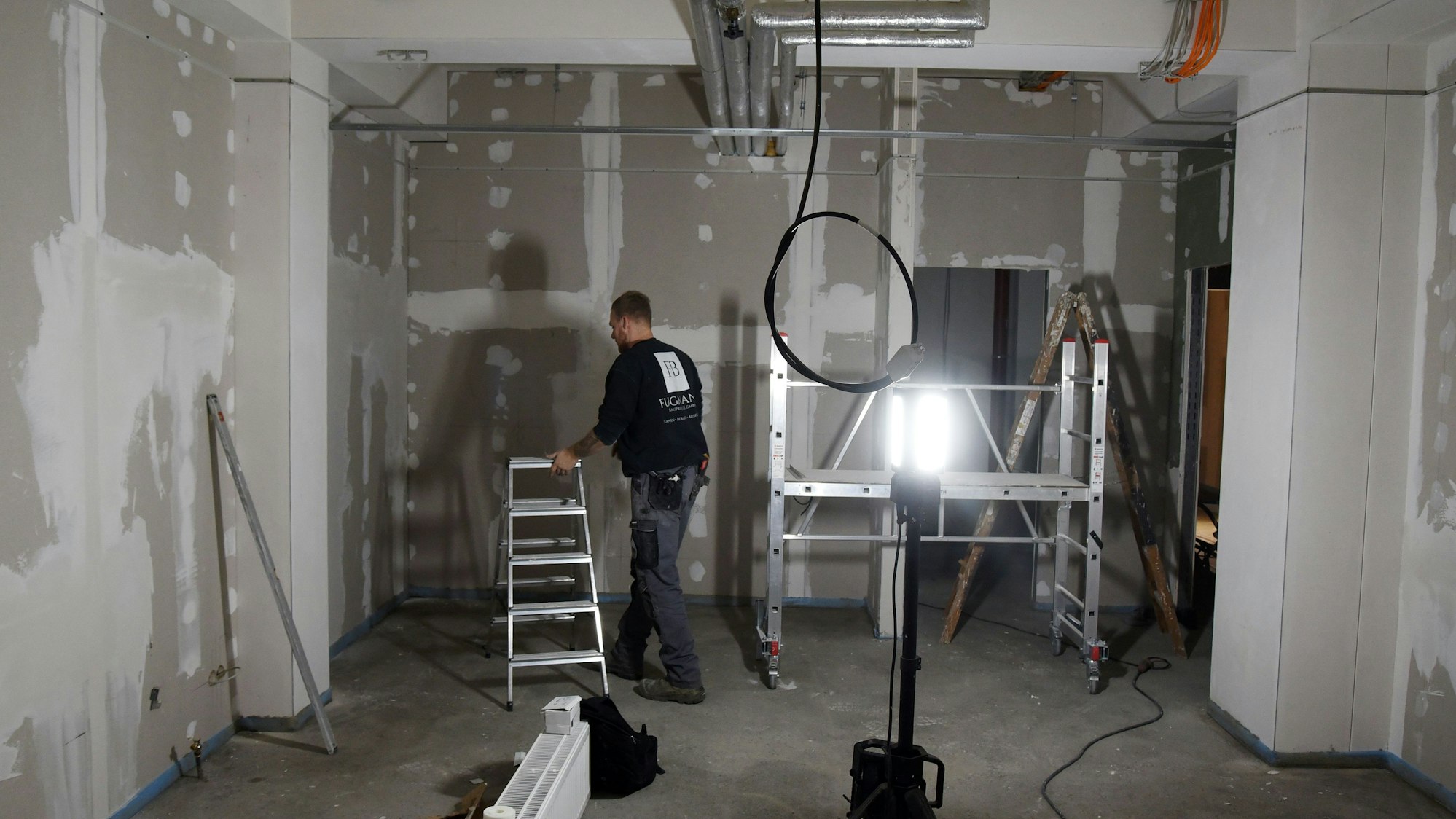 Blick auf einen Raum, in dem ein Handwerker gerade die Lampen montiert.