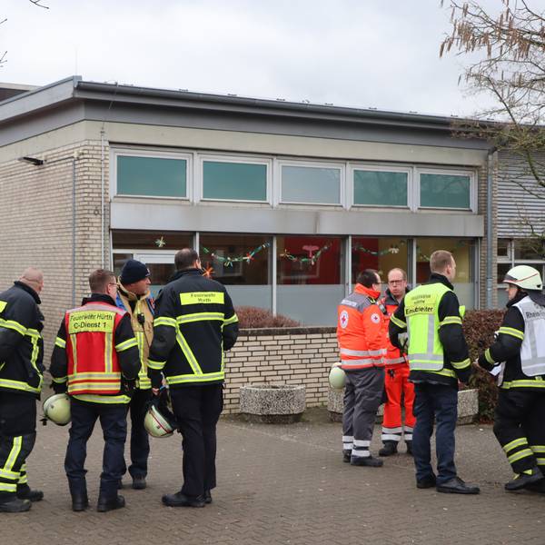 Fas Foto zeigt Einsatzkräfte und ein Einsatzfahrzeug der Feuerwehr vor dem Schulgebäude.