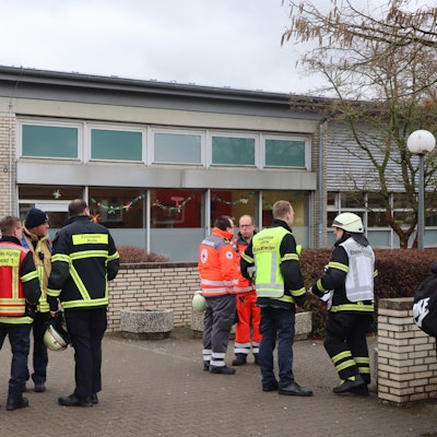 Fas Foto zeigt Einsatzkräfte und ein Einsatzfahrzeug der Feuerwehr vor dem Schulgebäude.