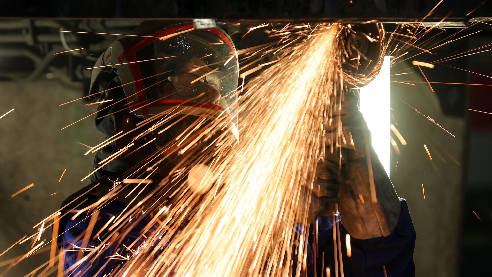 Ein Mitarbeiter eines Maschinenbauers schneidet mit einem Trennschleifer Metallteile aus einem Träger. Gerade in der Industrie ist die Stimmung gedämpft.