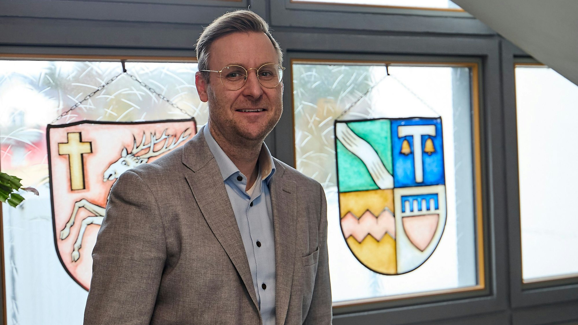 Martin Berners steht im Rathaus in Hellenthal an einem Fenster, das ein Wappen zeigt.