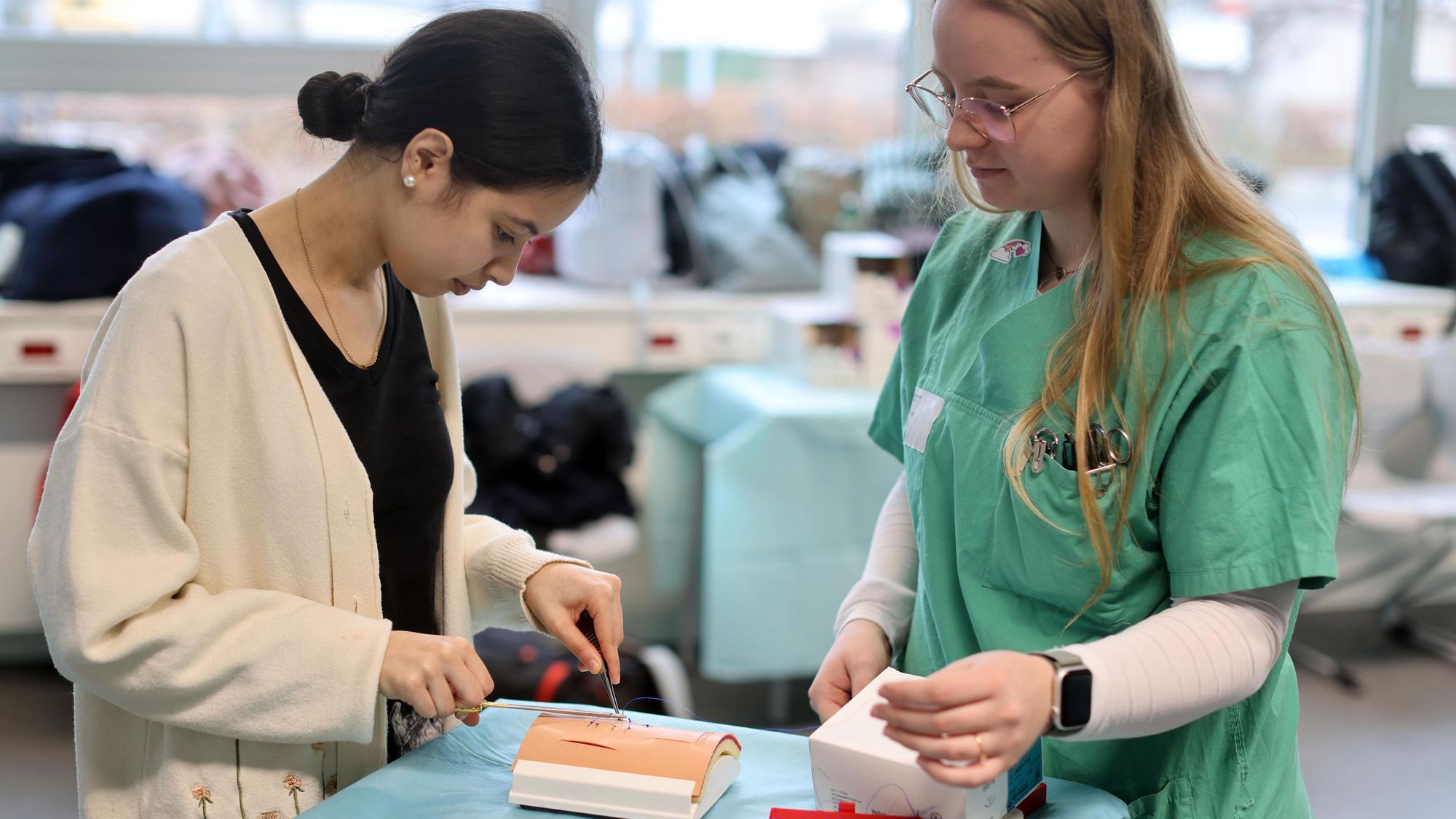 Schülerin Amina Gassa (l.) probiert in einem Workshop aus, wie Nähte gemacht werden. Geleitet wird er von Operationstechnischen Assistentinnen.