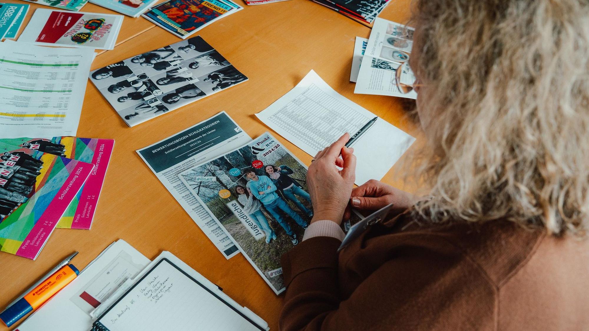 Das Foto zeigt eine Frau, die sich Printprodukte auf einem Tisch ansieht.