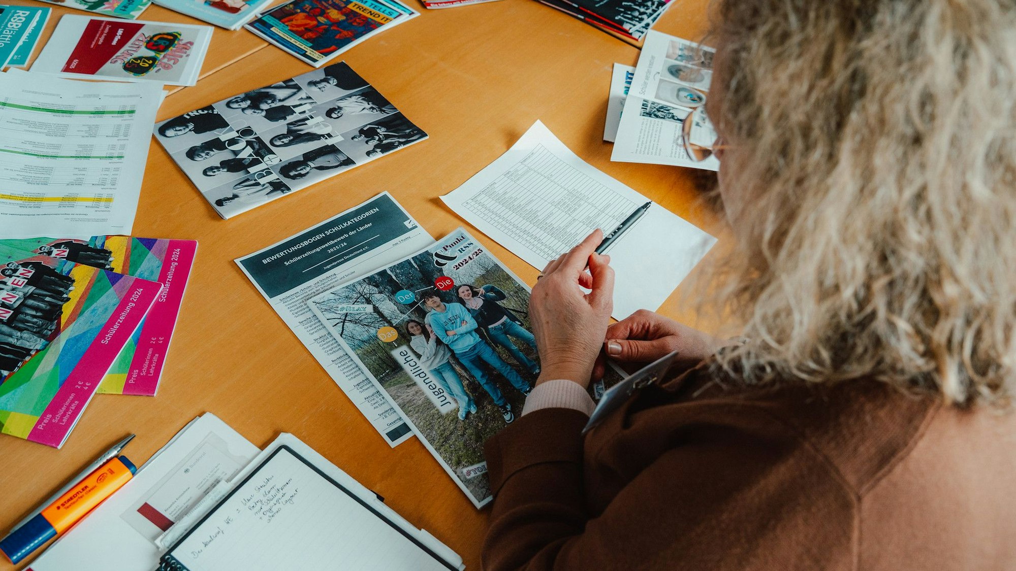 Das Foto zeigt eine Frau, die sich Printprodukte auf einem Tisch ansieht.