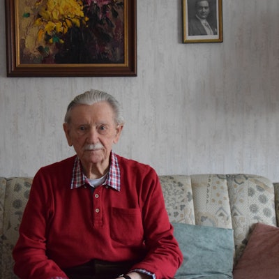 Ein Mann mit grauem Haar und Schnäuzer sitzt auf einem Sofa.