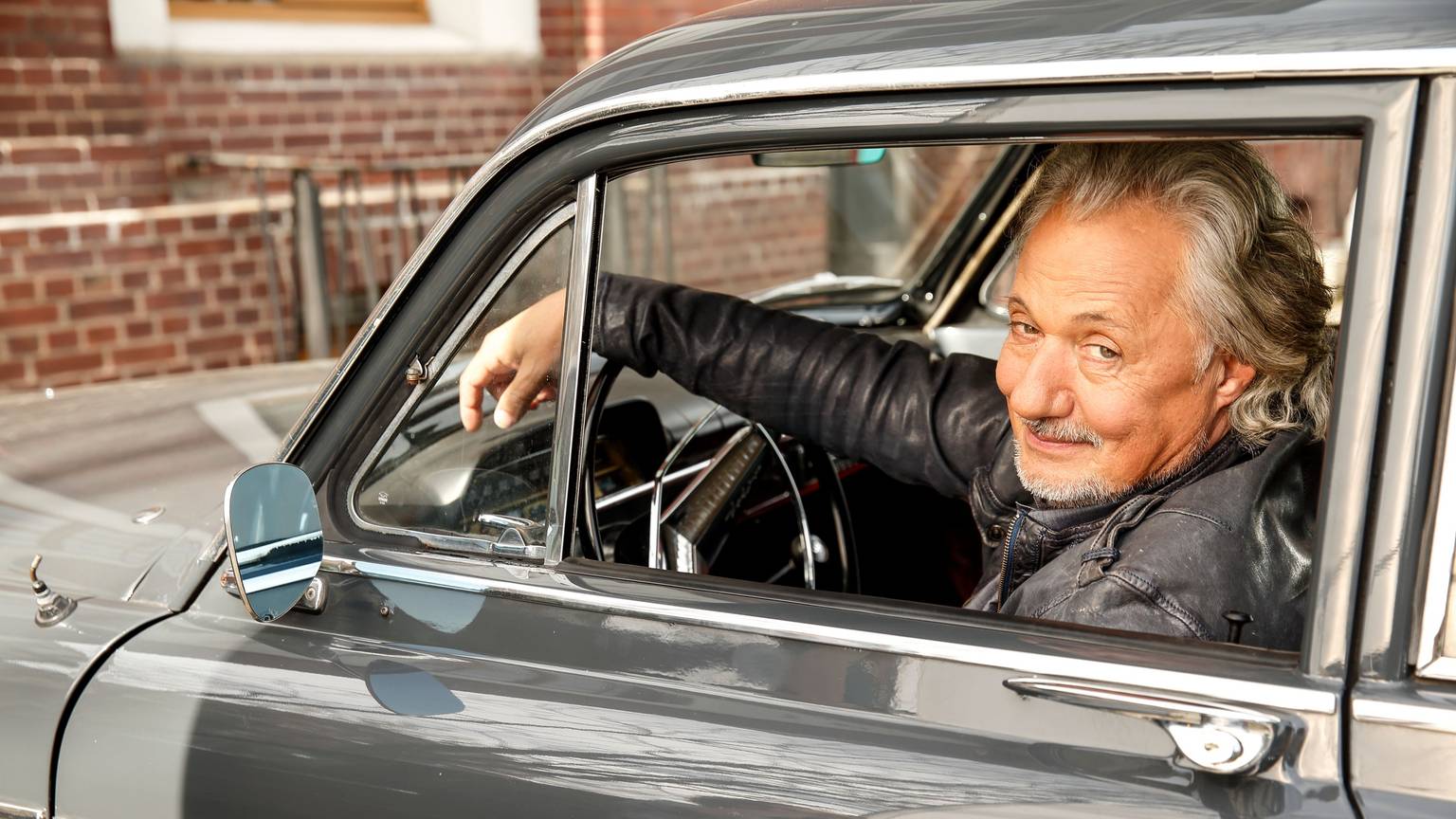 Konrad Beikircher am Steuer eines Autos.