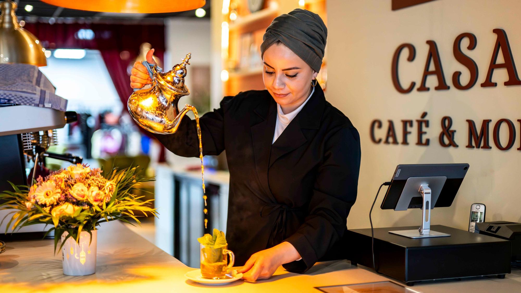 Das Bild zeigt Mahjouba Yasmine in ihrem Café an der Berliner Straße in Euskirchen. Sie gießt gerade einen Tee auf.