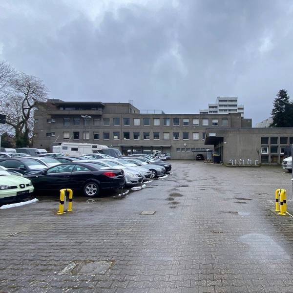 Zu sehen sind eine als Parkplatz genutzte Fläche sowie im Hintergrund Gebäude.