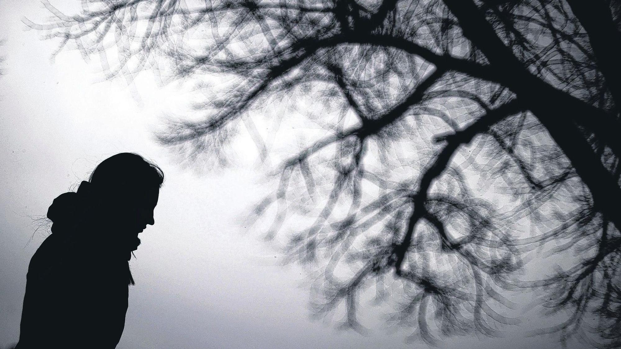Die Silhouette einer Frau vor der Silhouette eines blattlosen Baums.