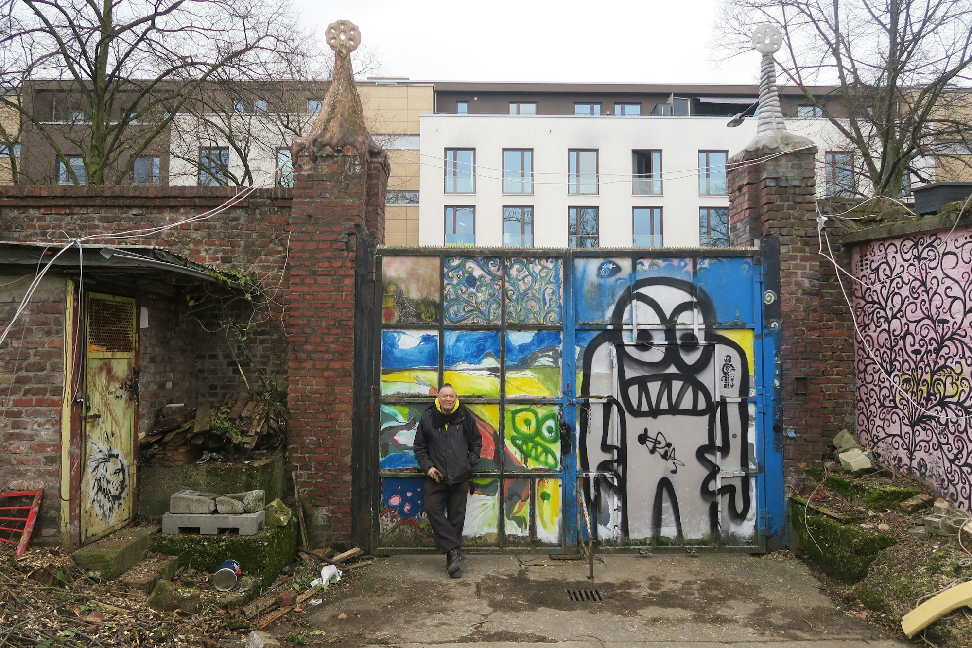 Ein Mann steht an ein Tor gelehnt. Darauf prangen Graffiti-Männchen.