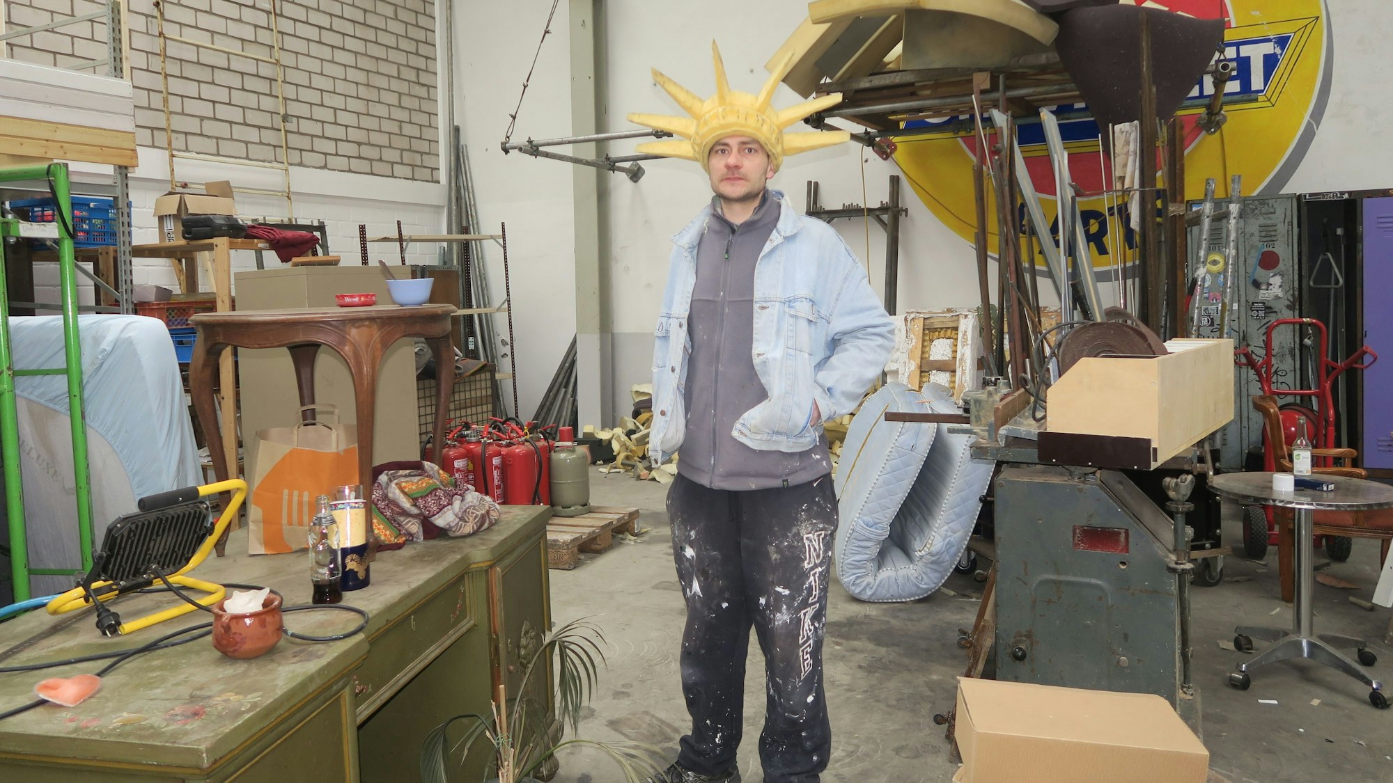 Ein Mann mit einem Sternenkranz auf dem Kopf steht in einer weitläufigen Werkstatt.