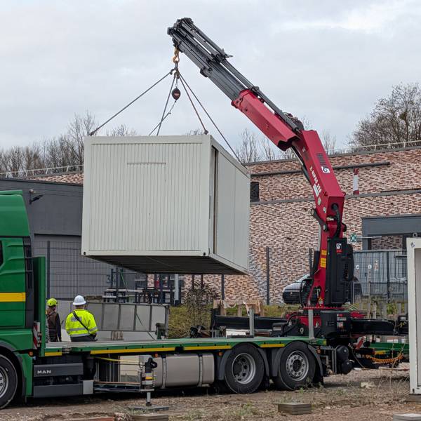 Das Foto zeigt die Verladung eines Baustellencontainers mit einem Autokran.