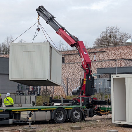 Das Foto zeigt die Verladung eines Baustellencontainers mit einem Autokran.