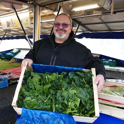 Markthändler Ugur Sezer zeigt eine Kiste mit frischem Spinat, typisch für den Winter.