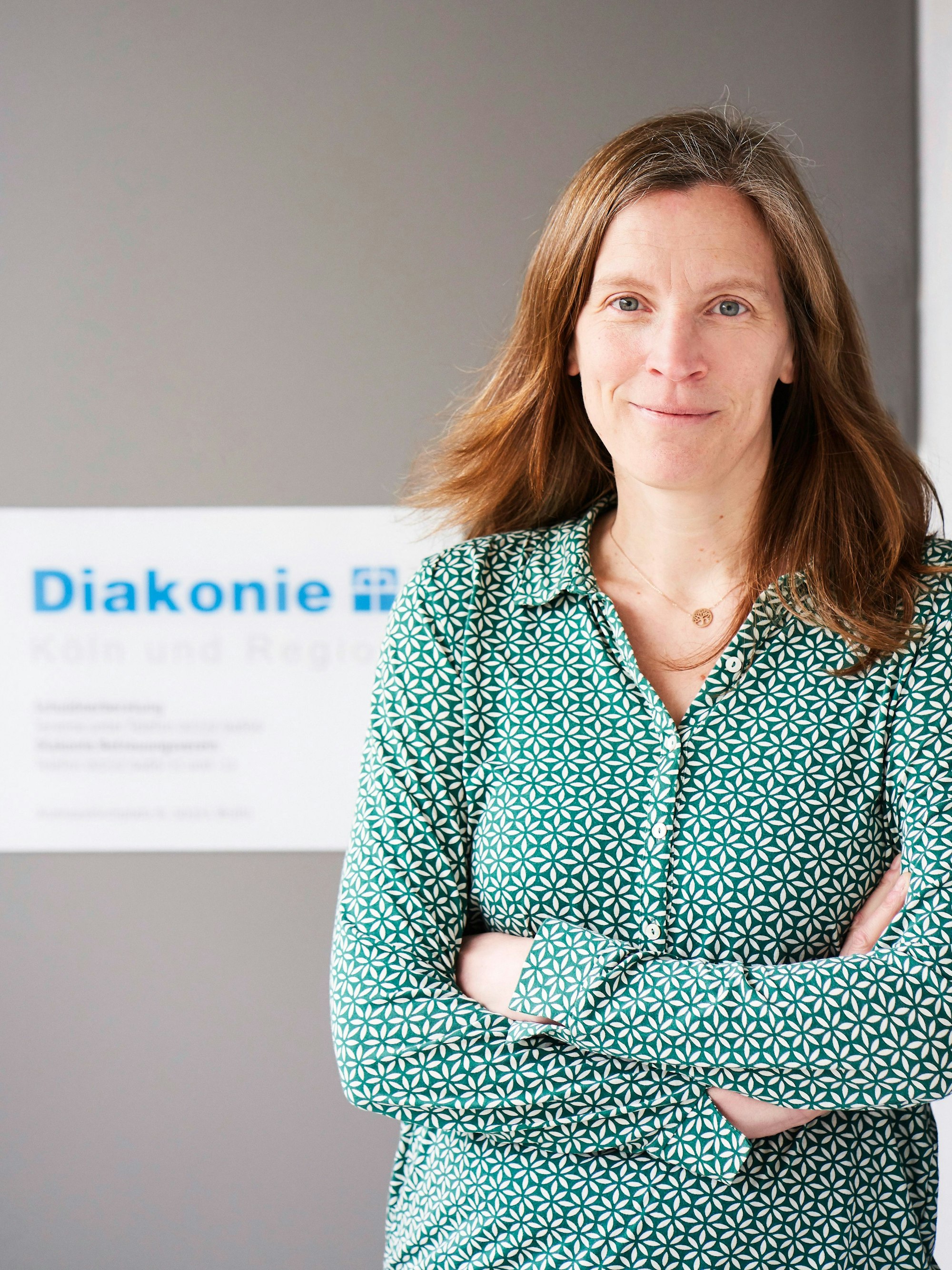 Eine Frau in grüner Bluse steht vor einem grauen Hintergrund.