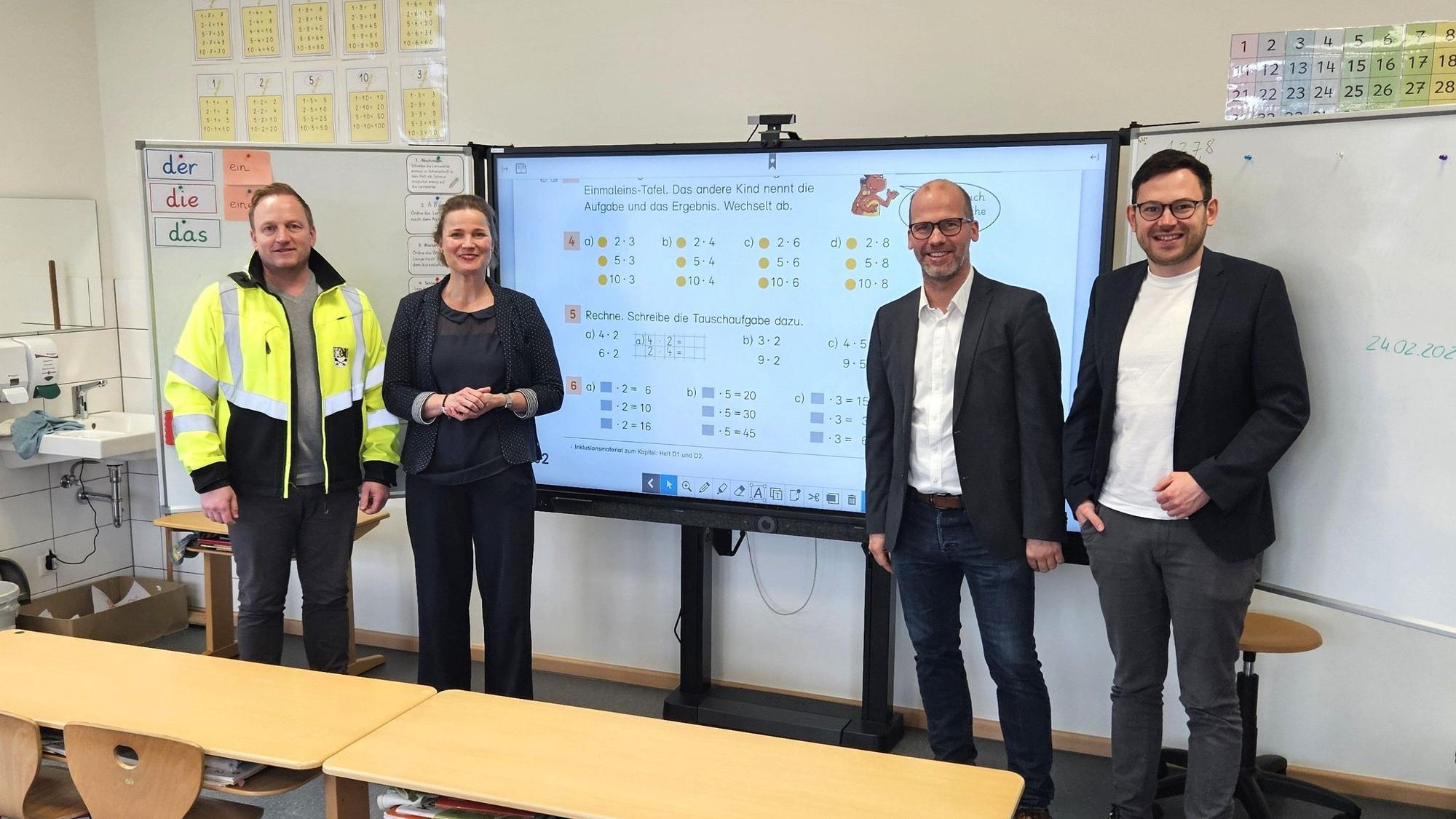 Stefan Etten (Bauamt), Maren Wessel (Schulleiterin), Markus Auel und Bürgermeister Emmanuel Kunz stehen nebeneinander vor einer digitalen Tafel.