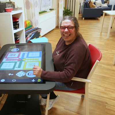 Auf dem Bild sind eine Frau und ein Mann zu sehen, die an einem digitalen Spieltisch sitzen.