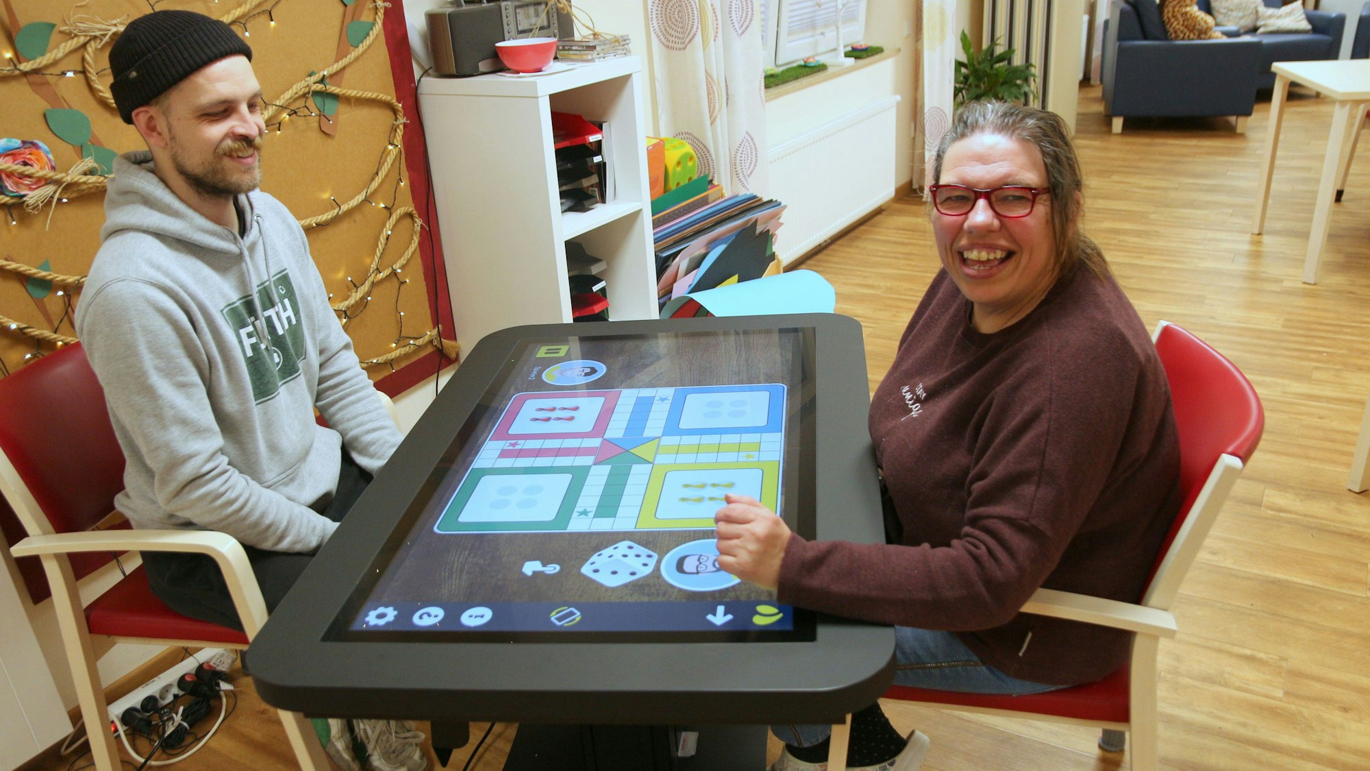 Auf dem Bild sind eine Frau und ein Mann zu sehen, die an einem digitalen Spieltisch sitzen.