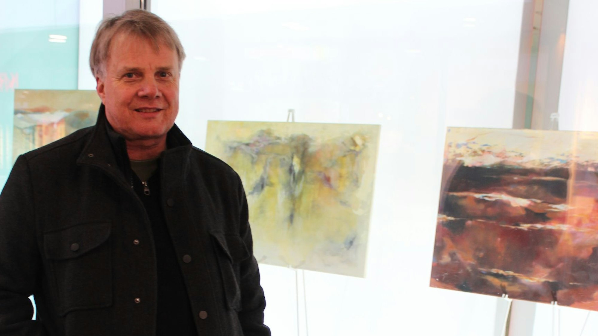 Ein Mann steht neben seinen ausgestellten Bildern.