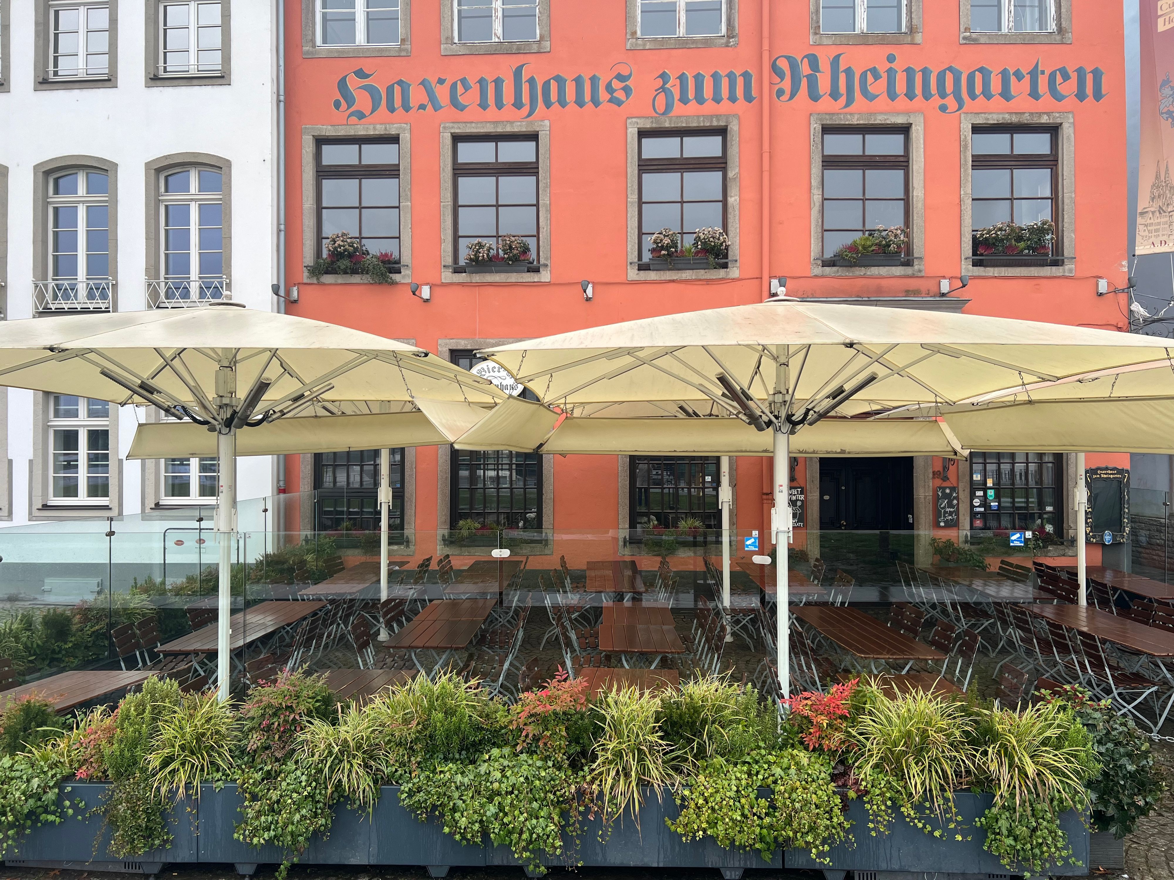 Am Haxenhaus werden transparente Glaselemente verwendet mit Blumenkästen und Sonnenschirmen verwendet.