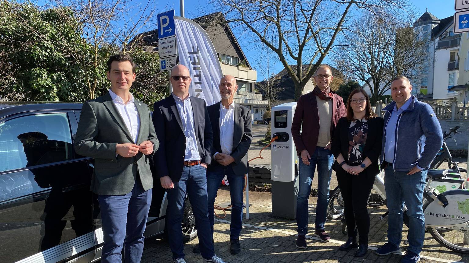 Sechs Menschen stehen neben einem Auto, im Hintergrund eine Ladesäule.