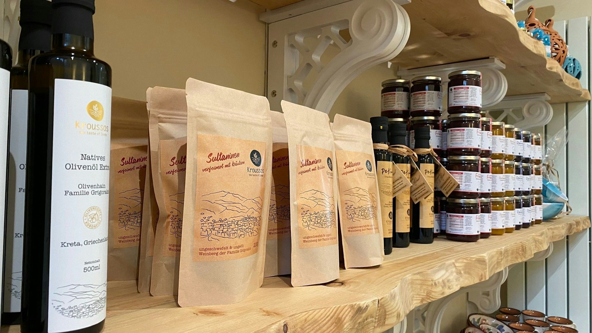 Zu sehen sind eine Olivenölflasche sowie Packungen mit Sultaninen und Gläser mit Honig.