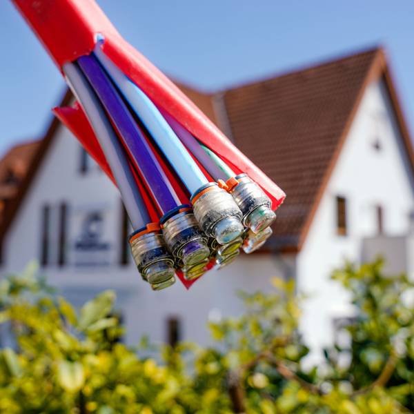 Das Symbolfoto zeigt Glasfaserkabel und im Hintergrund ein Einfamilienhaus.