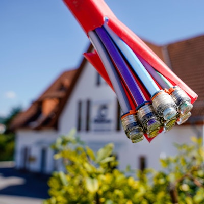 Das Symbolfoto zeigt Glasfaserkabel und im Hintergrund ein Einfamilienhaus.