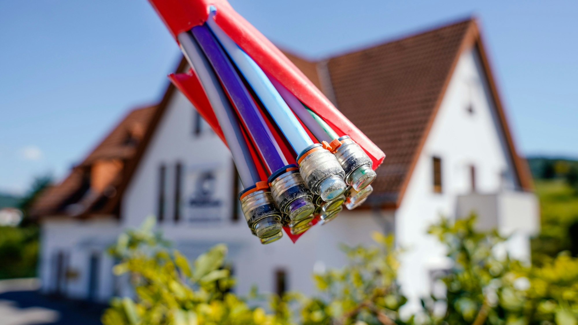 Das Bild zeigt eine aufgeschnittene Glasfaserleitung, im Hintergrund sieht man ein Einfamilienhaus.