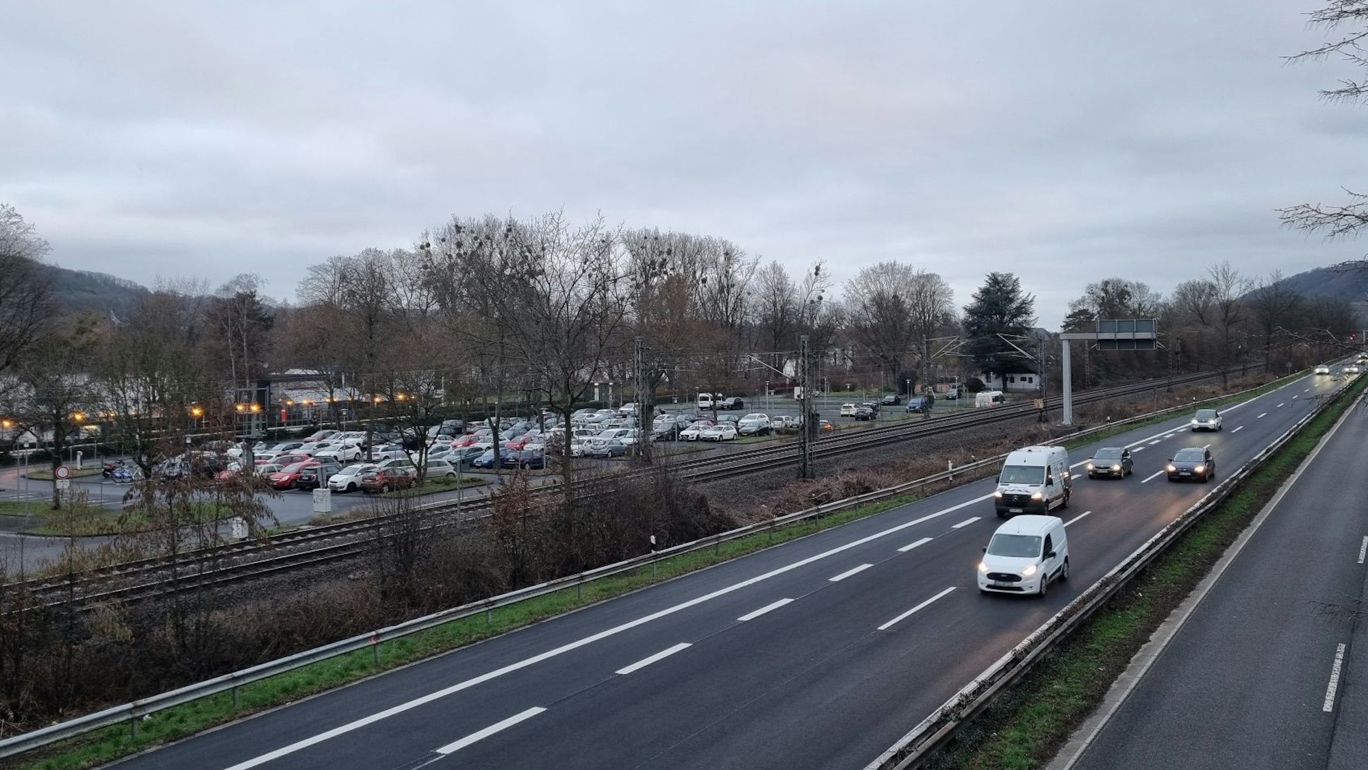 Ein Parkplatz, die Bahntrasse und Autos auf einer vierspurigen Straße.